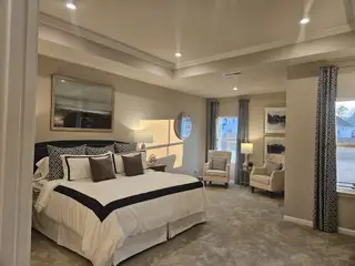 A spacious bedroom with elegant decor, featuring a plush bed, cozy seating area, and soft natural lighting through large windows.