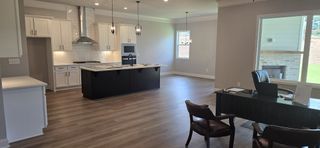 A spacious open-plan kitchen with white cabinetry, dark island, and elegant lighting, flowing into a cozy living area.