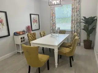 A chic dining room featuring a white table, yellow tufted chairs, floral curtains, and stylish artwork.