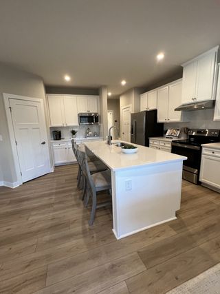Model Home A modern kitchen with white cabinetry, stainless steel appliances, and a central island with seating.
