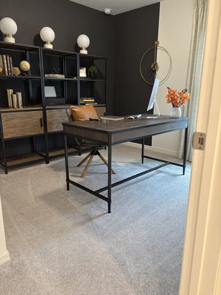 Model Home Modern office with sleek desk, dark shelving, globe decor, and accents in a cozy, carpeted space.