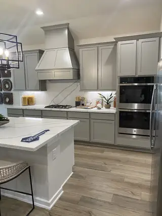 Model Home A modern kitchen with sleek gray cabinets, stainless steel appliances, and elegant wood flooring.