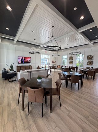 A spacious community room with elegant chandeliers, a coffered ceiling, and leather seating.