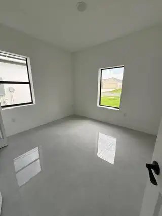 A bright room with glossy white floors, large windows, and minimalist white walls.