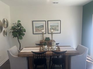 A cozy dining room with a wooden table, elegant décor, and wall art, complemented by natural light and a potted plant.