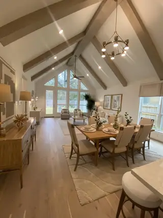 An elegant dining and living area with vaulted ceilings, wooden beams, and large windows for natural light.