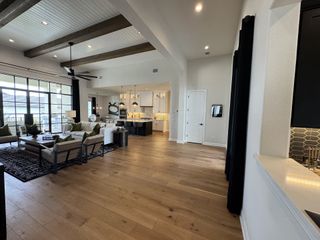 An open-concept living area with wood floors, exposed beams, and a bright kitchen.