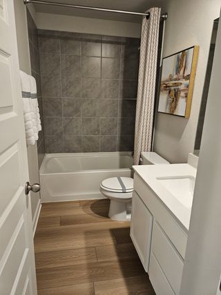 A modern bathroom featuring a gray tiled shower, wood-style flooring, and a white vanity for a clean, elegant look.