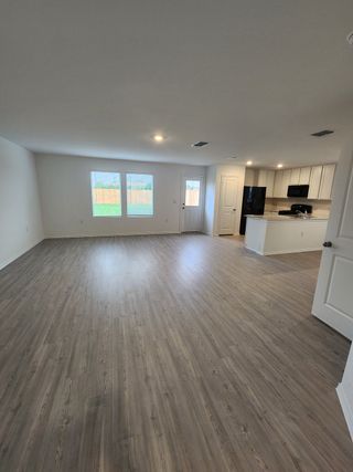 Model Home An open living area with sleek wood flooring, bright windows, and a modern kitchen featuring minimalist cabinetry.
