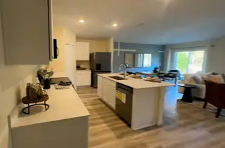 A modern kitchen with sleek white cabinetry, a spacious island, and open layout connecting to a cozy living room.