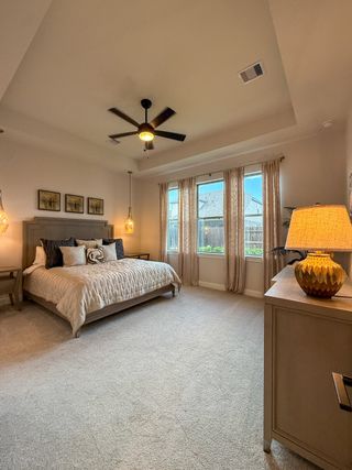 A cozy bedroom with a plush bed, soft lighting, large windows, and a ceiling fan exuding warmth and comfort.