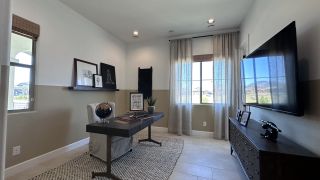A modern home office with a sleek desk, wall-mounted TV, elegant decor, and natural light streaming through sheer curtains.