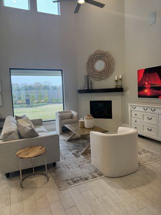 Model Home A cozy living room with high ceilings, modern fireplace, neutral furniture, and large windows opening to a serene backyard view.