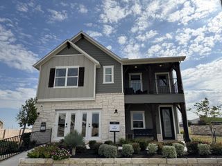 A charming two-story home with elegant stone facade and balcony in Covered Bridge by Ashton Woods (Hutto, TX).