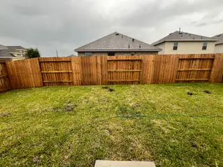 Model Home A private backyard with a tall wooden fence, lush green grass, and plenty of space for outdoor activities.