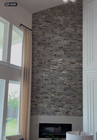 Model Home A grand living room with a floor-to-ceiling stone accent wall and large windows, providing an airy and elegant atmosphere.