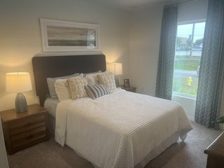 A cozy bedroom featuring a plush bed with textured pillows, wooden nightstands, and elegant curtains allowing natural light in.