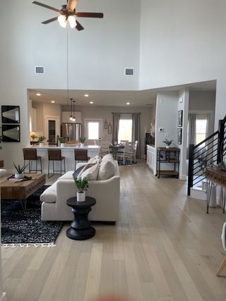 A spacious living room with high ceilings, light wood floors, modern furnishings, and an open-plan kitchen area.