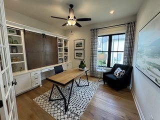 Model Home A cozy home office with a wooden desk, white built-in shelves, and a dark armchair on a patterned rug.