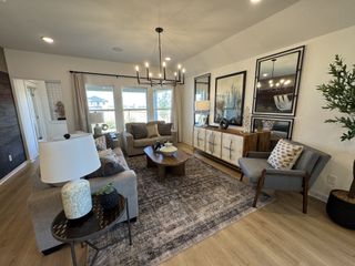 Model Home A cozy living room with a modern chandelier, neutral sofas, patterned rug, and large windows providing ample natural light.