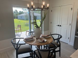A cozy dining area with a round wooden table, modern chairs, and a chic chandelier overlooking a lush backyard.