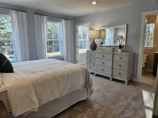 A spacious bedroom with plush carpeting, soft blue walls, large windows, and elegant furniture for a serene retreat.