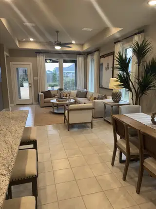 A spacious living area with neutral tones, tiled floor, and ample natural light, featuring cozy seating and a dining space.