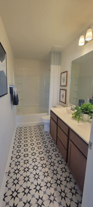 A stylish bathroom in a Medina Crossing home, featuring unique star-patterned tile flooring, a combination tub and shower, and a modern vanity with dual sinks (Von Ormy, TX).