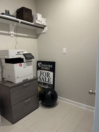 A compact office nook featuring a printer, storage cabinet, and wall shelving for organized functionality.
