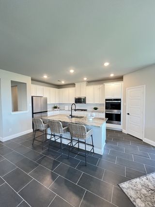 Model Home A modern kitchen with sleek gray tile flooring, white cabinetry, and a spacious marble island with stylish woven chairs.