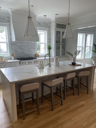 A modern kitchen with a marble island, elegant pendant lights, and a light wood floor.