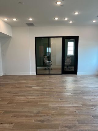 A spacious room with wooden flooring, recessed lighting, and modern glass doors leading to a cozy office space.