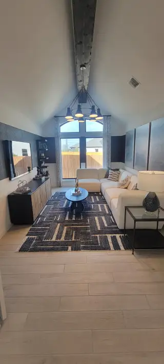 A cozy living room with a vaulted ceiling, modern lighting, plush sofa, geometric rug, and sleek decor.