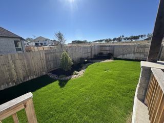 Street view A lush green backyard with a privacy fence in The Cottages at La Cima by Ashton Woods (San Marcos, TX).