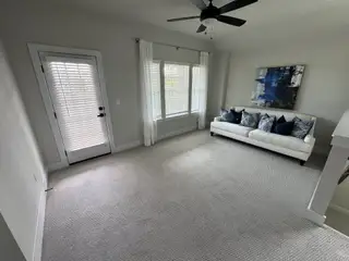 A cozy living room with a plush sofa, decorative pillows, and large windows with blinds for natural light.