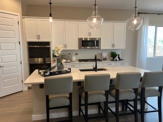 A sleek kitchen featuring a large island, pendant lights, white cabinets, and stainless steel appliances.