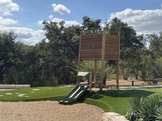 A charming playground with a wooden slide set amidst lush greenery in Wolf Ranch: 46ft. lots by Highland Homes (Georgetown, TX).