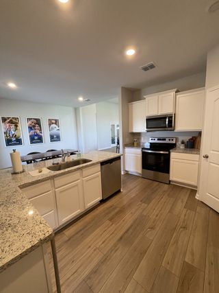 A modern kitchen with wood floors, granite countertops, stainless steel appliances, and white cabinetry.