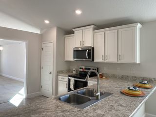 A modern kitchen with sleek white cabinets, marbled countertops, stainless steel appliances, and recessed lighting.