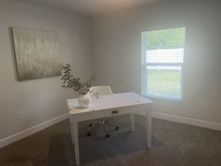 Model Home A cozy office with neutral walls, a white desk, and a modern chair, featuring a large window and stylish decor.