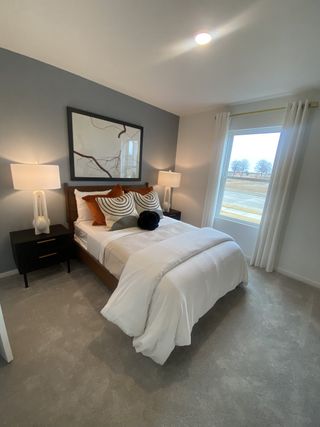 A cozy bedroom with soft gray walls, modern artwork, plush bedding, and natural light from a large window.