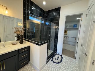 A chic bathroom with a glass-enclosed shower, black tile, elegant vanity, and geometric flooring.