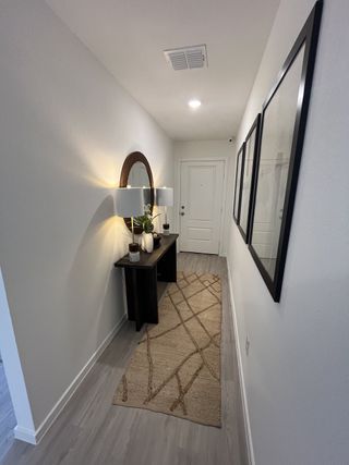 A welcoming hallway with sleek flooring, a stylish console, and warm lighting. Decor includes a round mirror and framed art.