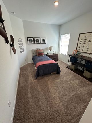 A cozy bedroom featuring a single bed, plush carpet, and charming decor with personal touches and natural light.