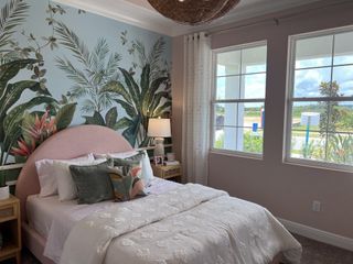 A cozy bedroom with a tropical mural, soft pink headboard, and large windows for natural light.
