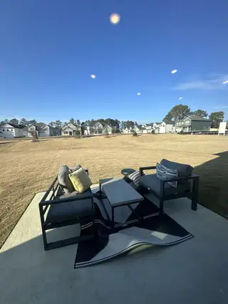 A cozy patio setup with modern seating and a view of a spacious backyard under a clear blue sky.