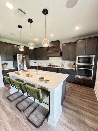 A modern kitchen with dark cabinets, an island with bar seating, pendant lights, and stainless steel appliances.
