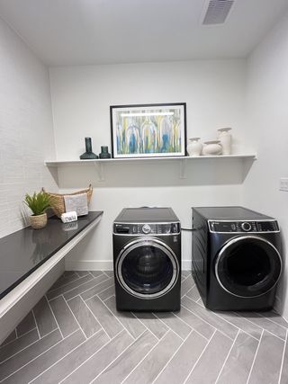 A sleek laundry room featuring modern black appliances, herringbone tile flooring, and elegant white shelving.