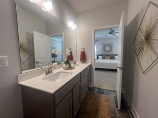 A modern bathroom with a sleek double vanity, large mirror, and stylish decor leading into a cozy bedroom.