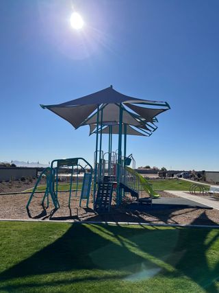 A sunny playground with shade structures and play equipment in The Enclave on Olive by Meritage Homes (Waddell, AZ).